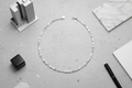 Silver necklace on a gray surface with office supplies in the background, white and silver