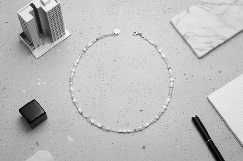 Silver necklace on a gray surface with office supplies in the background, white and silver