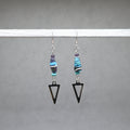 Pair of earrings with beaded elements and black triangle shapes on a gray background, paper beads from Ouganda with stainless steel