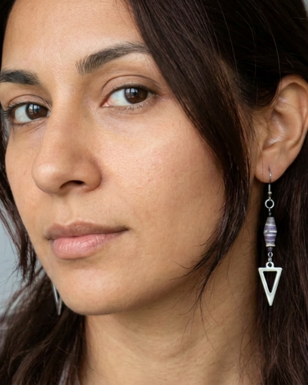 Close-up of a woman wearing a unique earring with a triangle design. Arrows silver with paper beads from Africa