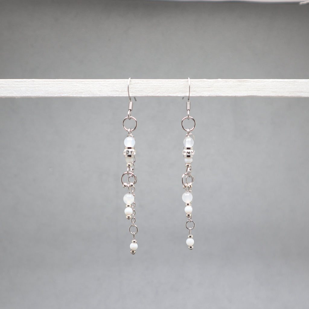 Pair of silver earrings with small beads on a gray background, white and silver