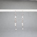Pair of silver earrings with small beads on a gray background, white and silver