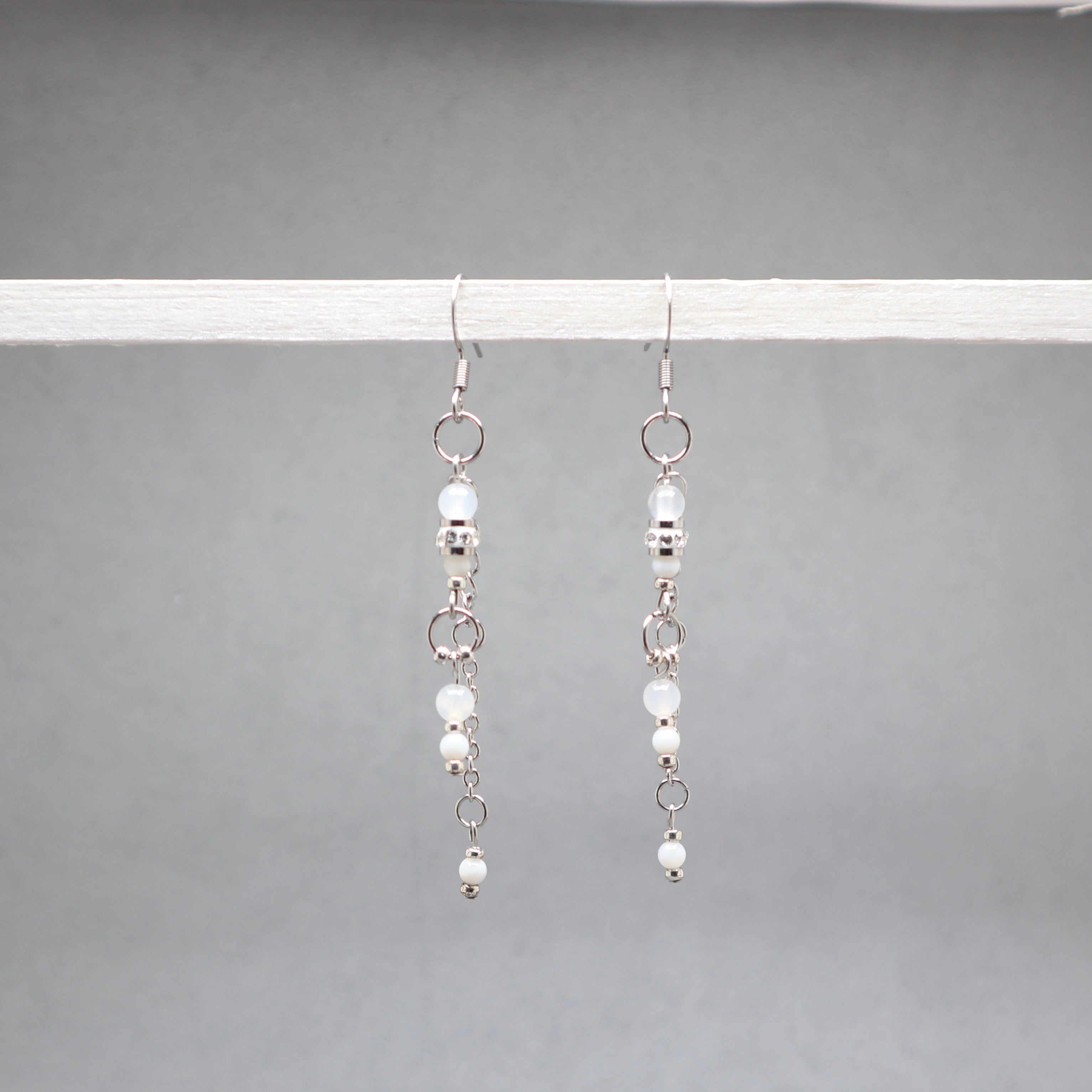 Pair of silver earrings with small beads on a gray background, white and silver