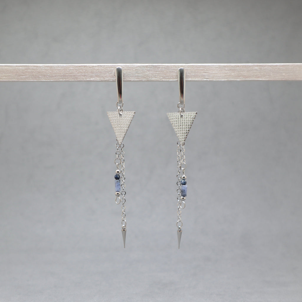 Pair of silver triangle earrings with chain and bead details on a gray background