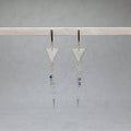 Pair of silver triangle earrings with chain and bead details on a gray background