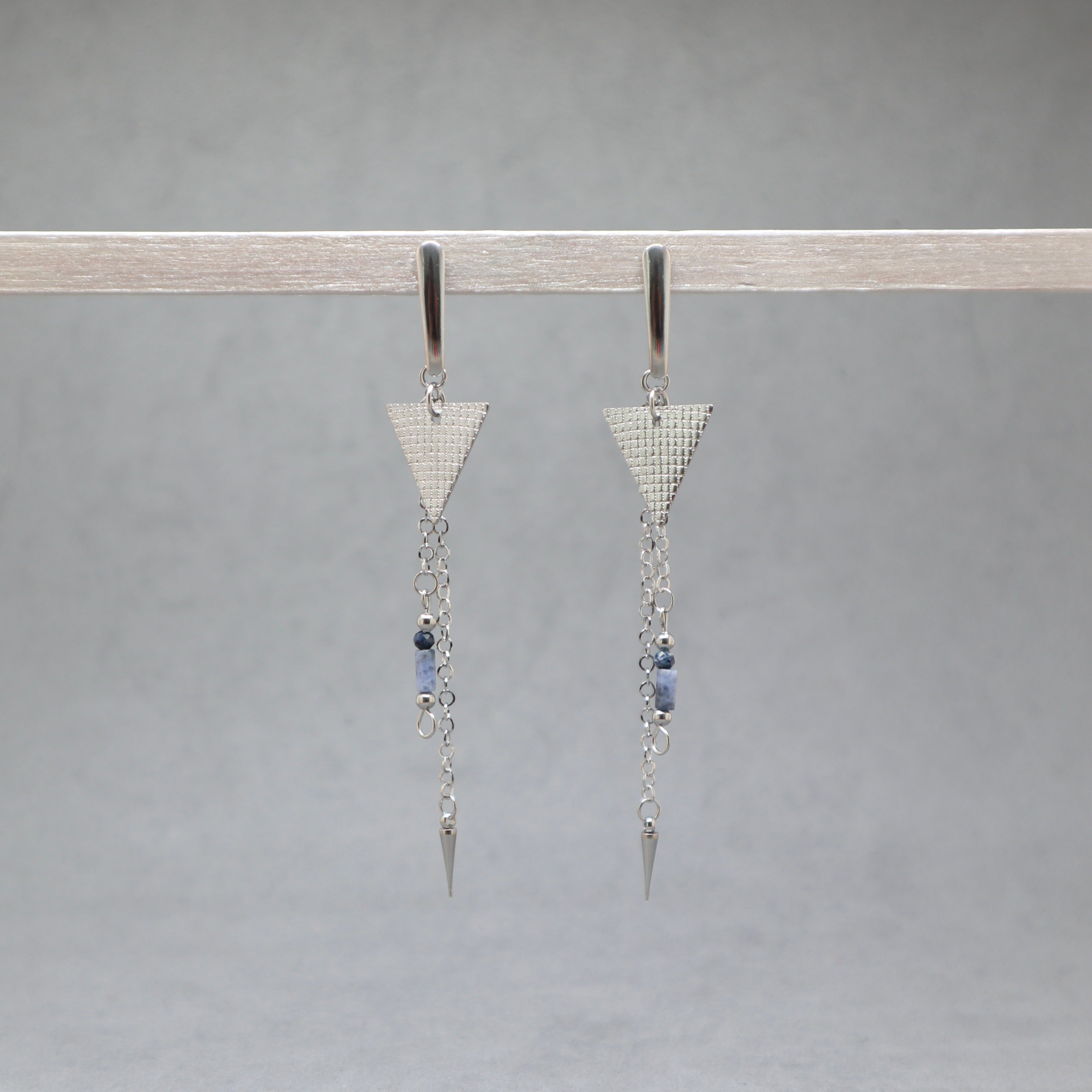 Pair of silver triangle earrings with chain and bead details on a gray background