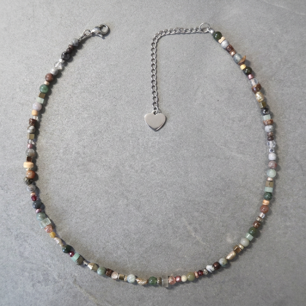 A beaded necklace with small multicolored gemstone beads and a silver heart-shaped pendant on a silver chain, displayed on a gray textured surface.