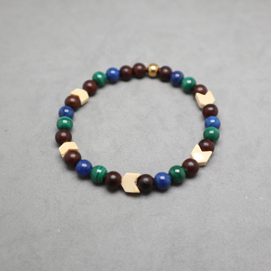A beaded stretch bracelet featuring dark brown wooden beads, blue and green stone beads, and light beige geometric wooden accents, displayed on a neutral gray background. Lapis, malachite, snake agate and wood.