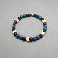 A beaded stretch bracelet featuring dark brown wooden beads, blue and green stone beads, and light beige geometric wooden accents, displayed on a neutral gray background. Lapis, malachite, snake agate and wood.