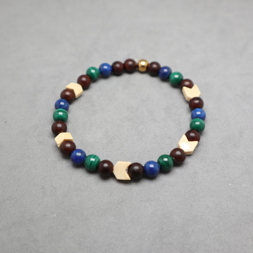A beaded stretch bracelet featuring dark brown wooden beads, blue and green stone beads, and light beige geometric wooden accents, displayed on a neutral gray background. Lapis, malachite, snake agate and wood.
