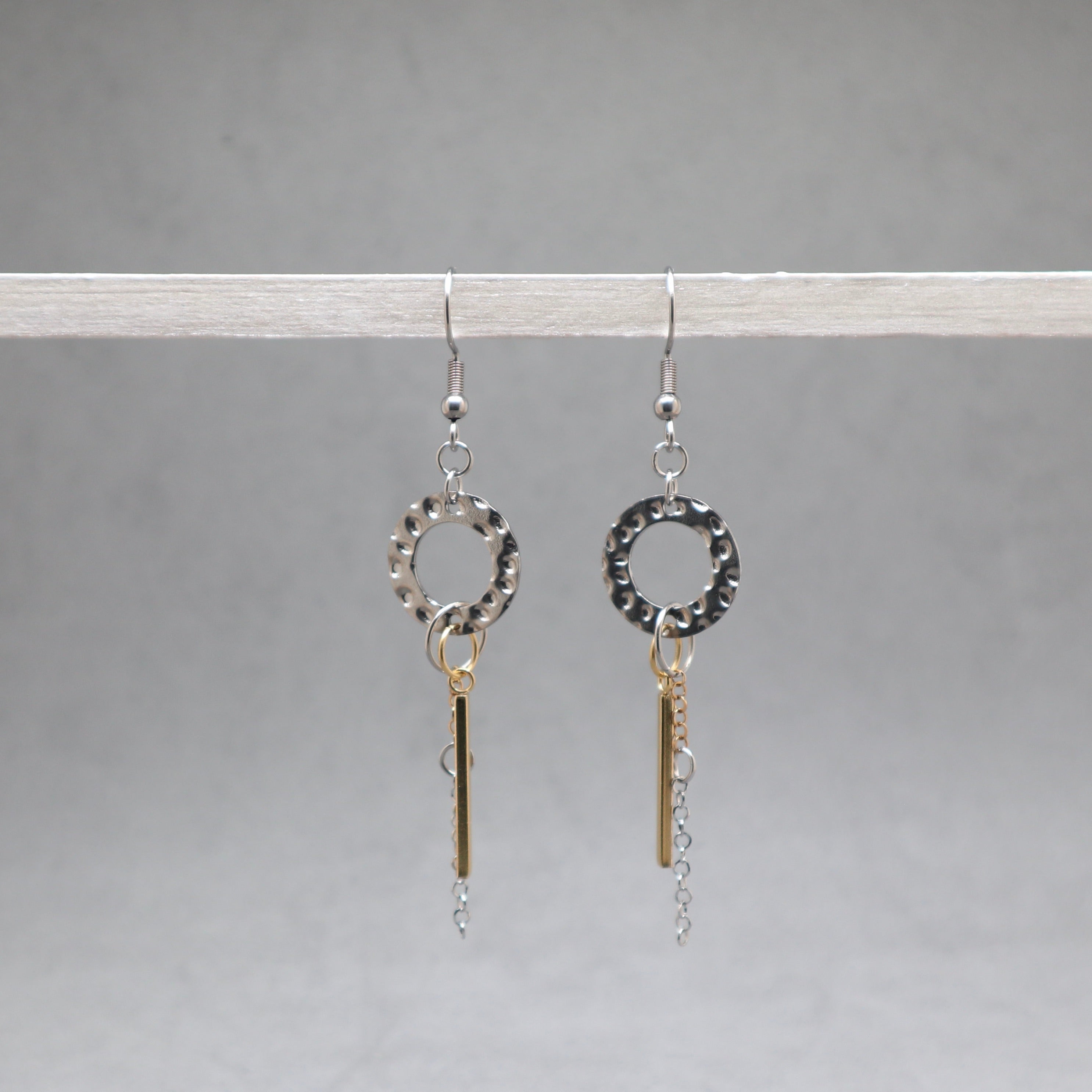 Pair of silver earrings with circular designs and hanging bars on a gray background