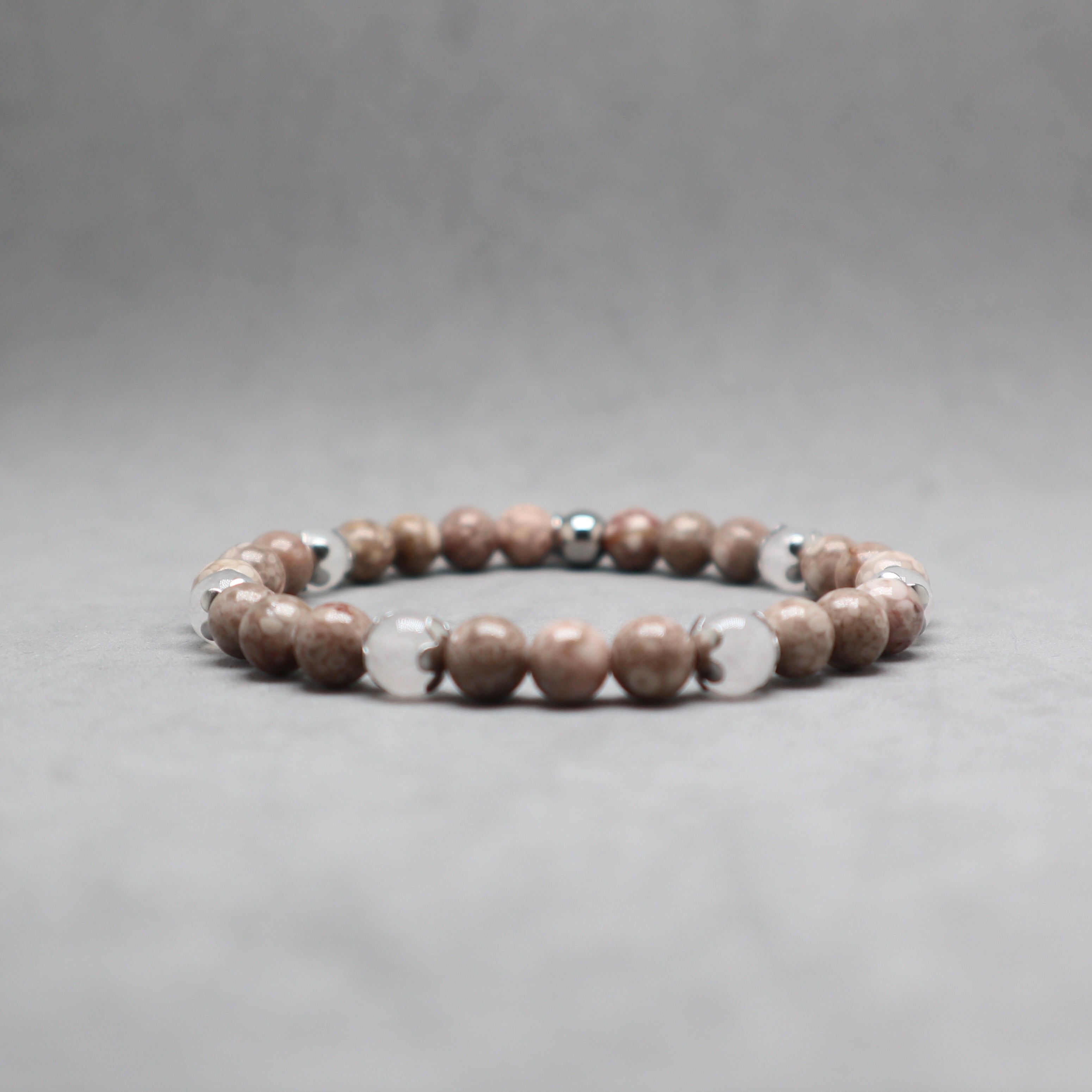 A beaded stretch bracelet featuring round brown and beige stone beads with a few polished silver metallic accent beads, displayed on a neutral gray background.