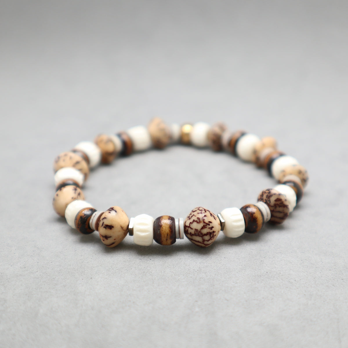 A beaded stretch bracelet made of alternating cream, brown, and dark brown marbled beads, displayed on a neutral gray background.