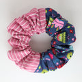 Two colors scrunchies, one pink with white stripes and the other blue with colorful patterns, on a light gray background.
