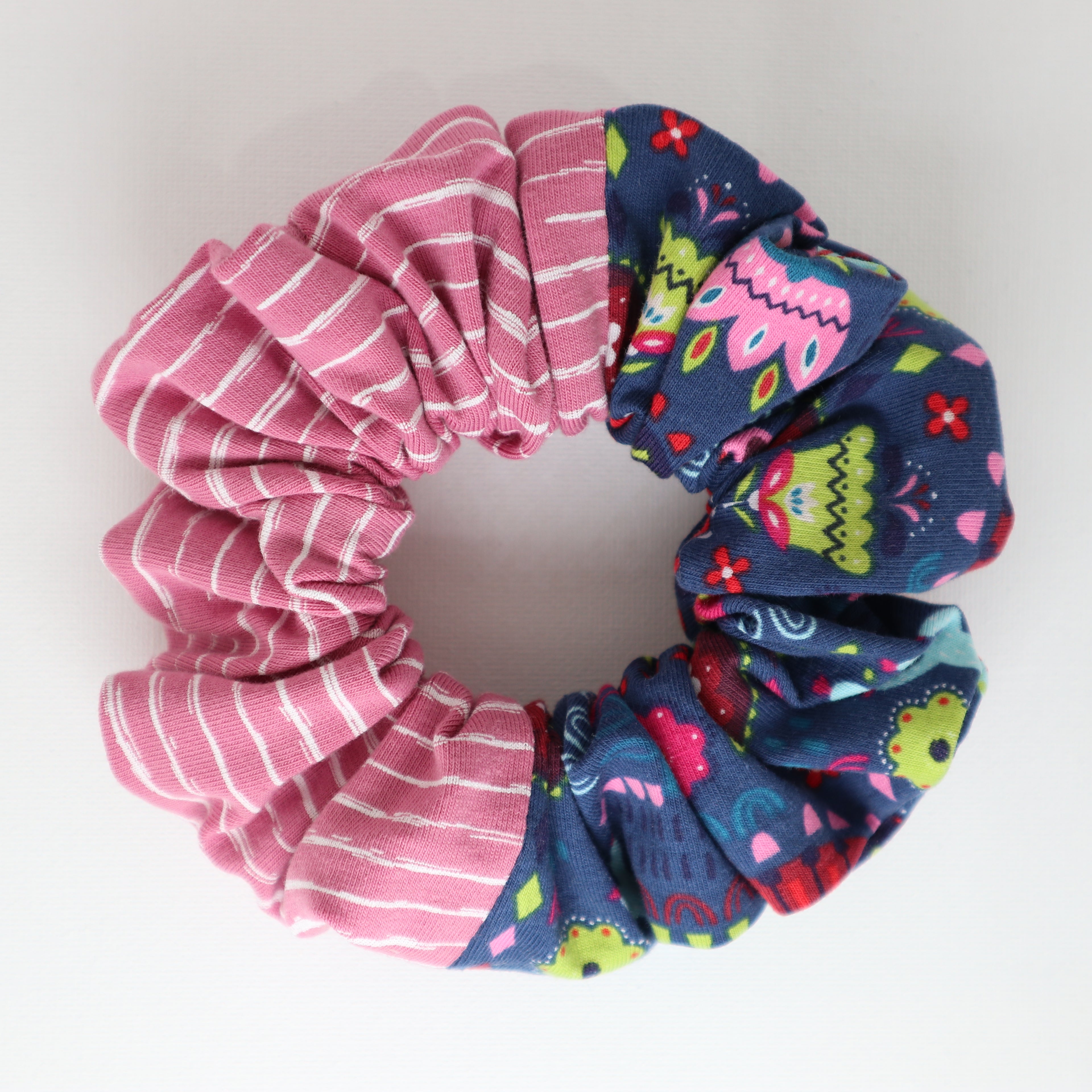 Two colors scrunchies, one pink with white stripes and the other blue with colorful patterns, on a light gray background.
