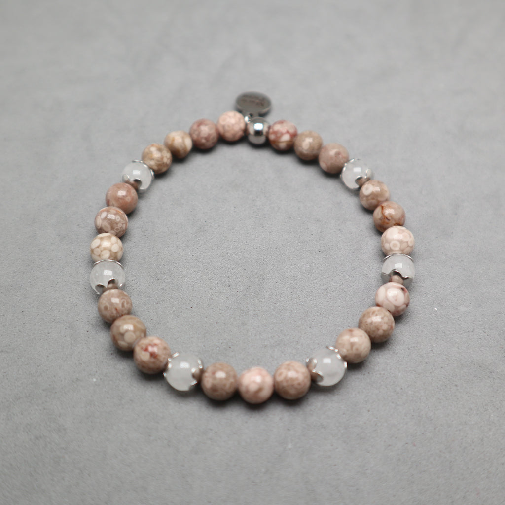A beaded stretch bracelet featuring round brown and beige stone beads, clear faceted beads, and a small silver spacer, displayed on a textured gray background. Maifanite and jade