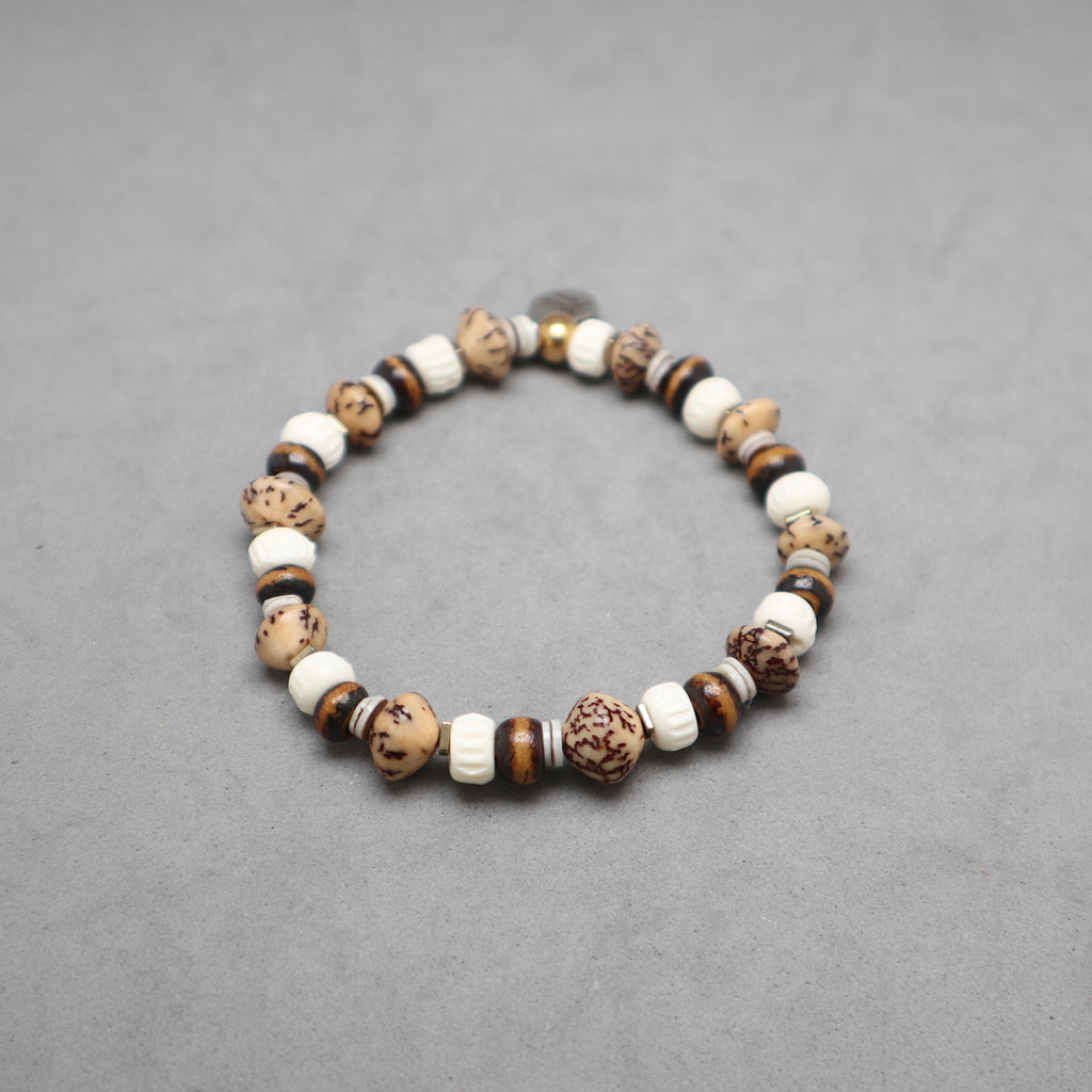 A beaded stretch bracelet made of natural wood, stone, and ceramic beads in earthy brown, beige, and white tones, displayed on a neutral gray background.