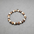 A beaded stretch bracelet made of natural wood, stone, and ceramic beads in earthy brown, beige, and white tones, displayed on a neutral gray background.