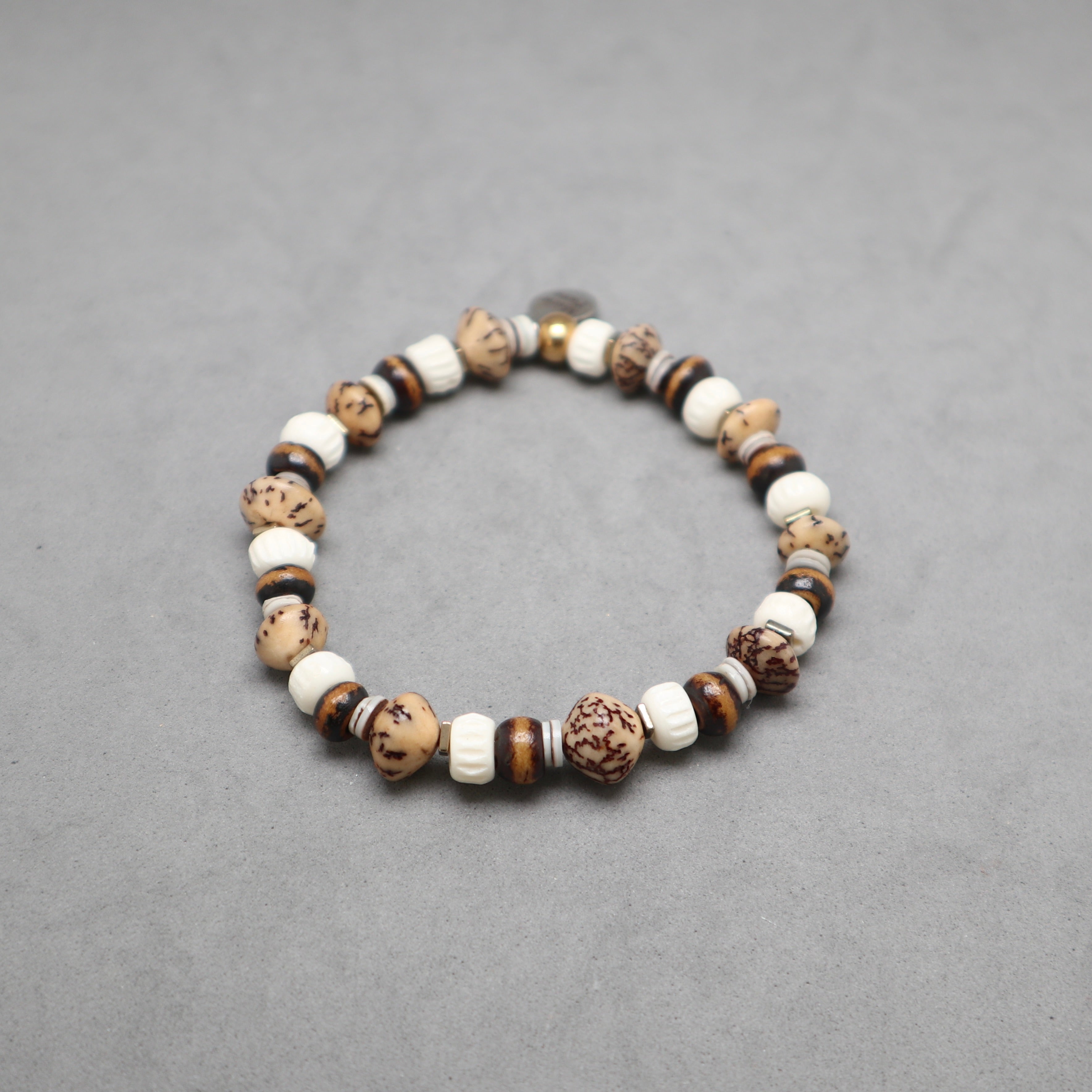 A beaded stretch bracelet made of natural wood, stone, and ceramic beads in earthy brown, beige, and white tones, displayed on a neutral gray background.
