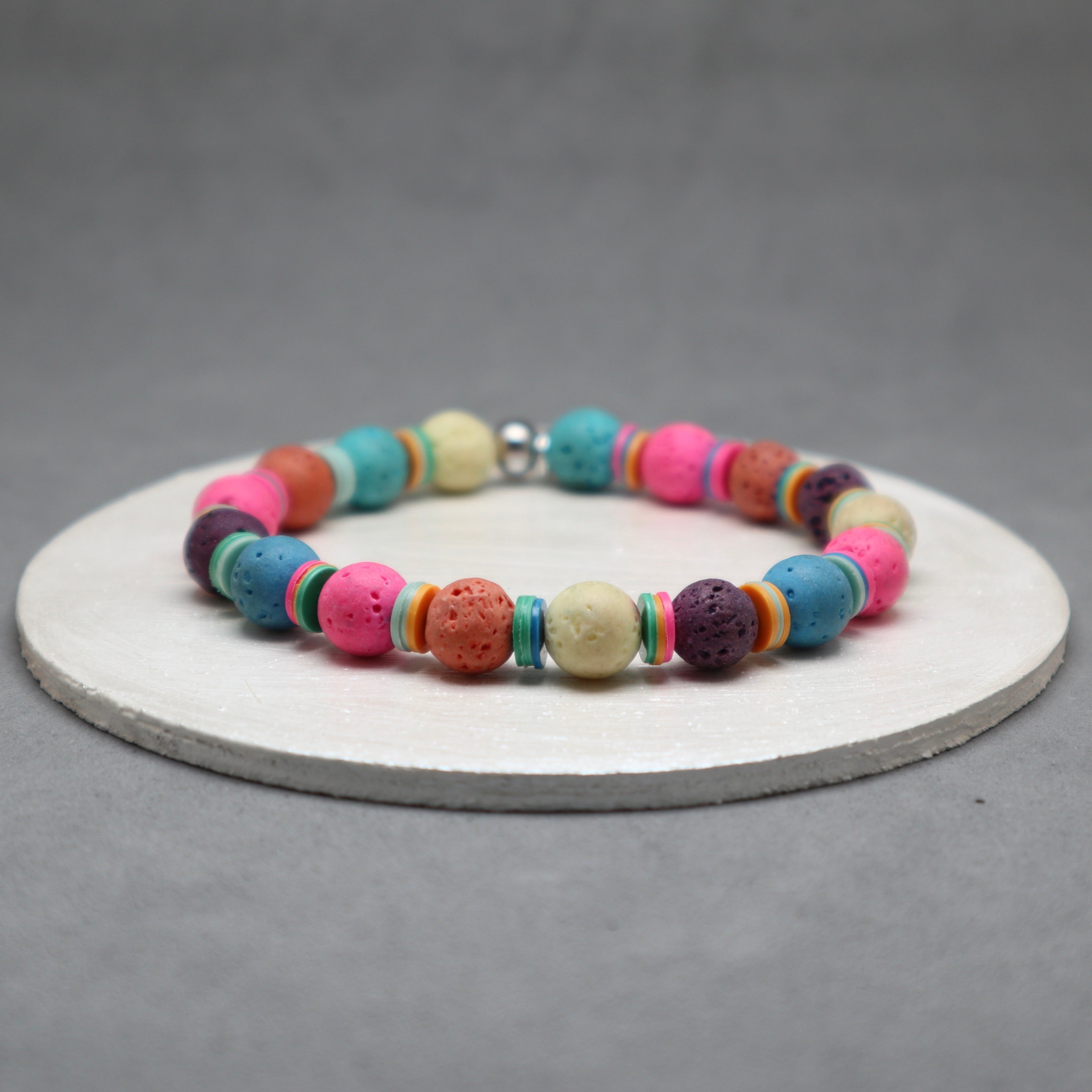 Colorful beaded bracelet on a white circular stand with a gray background, colorful lava, disk heishi