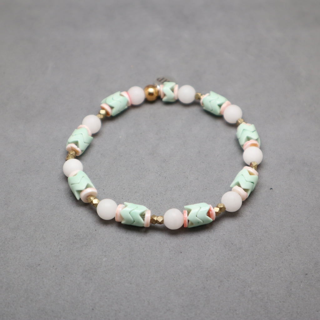 Beaded bracelet with green, white, and gold beads on a gray background