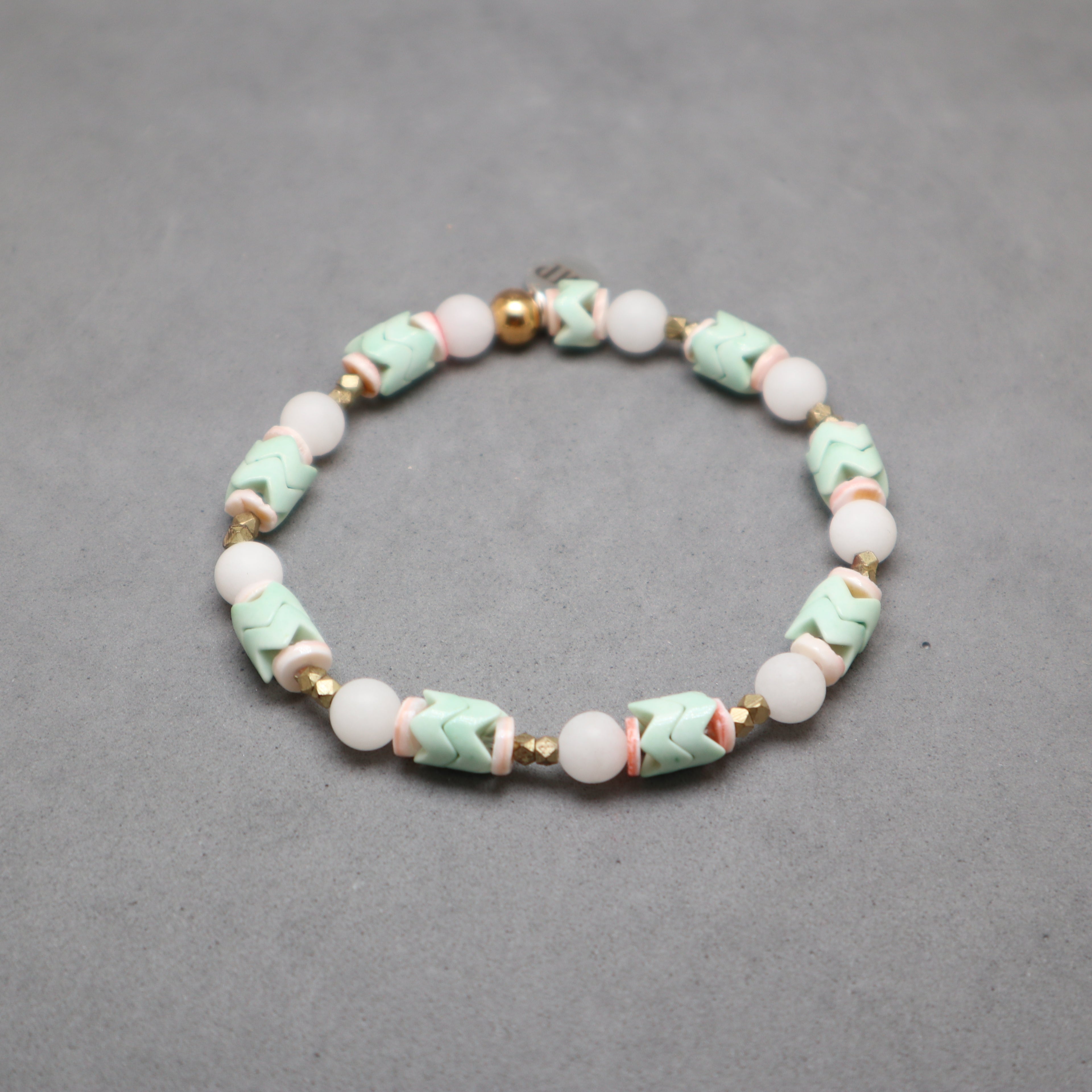 Beaded bracelet with green, white, and gold beads on a gray background