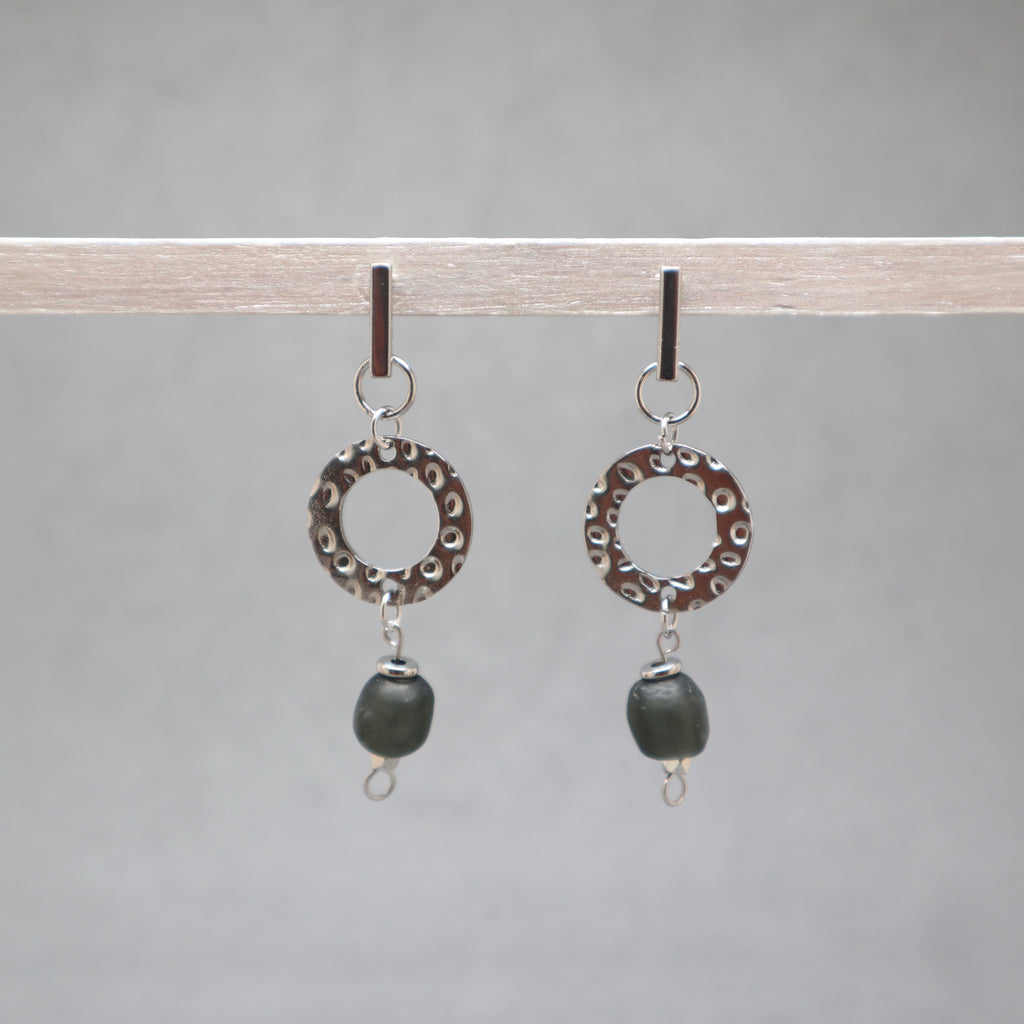 Pair of earrings with circular designs and black beads on a gray background