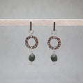 Pair of earrings with circular designs and black beads on a gray background