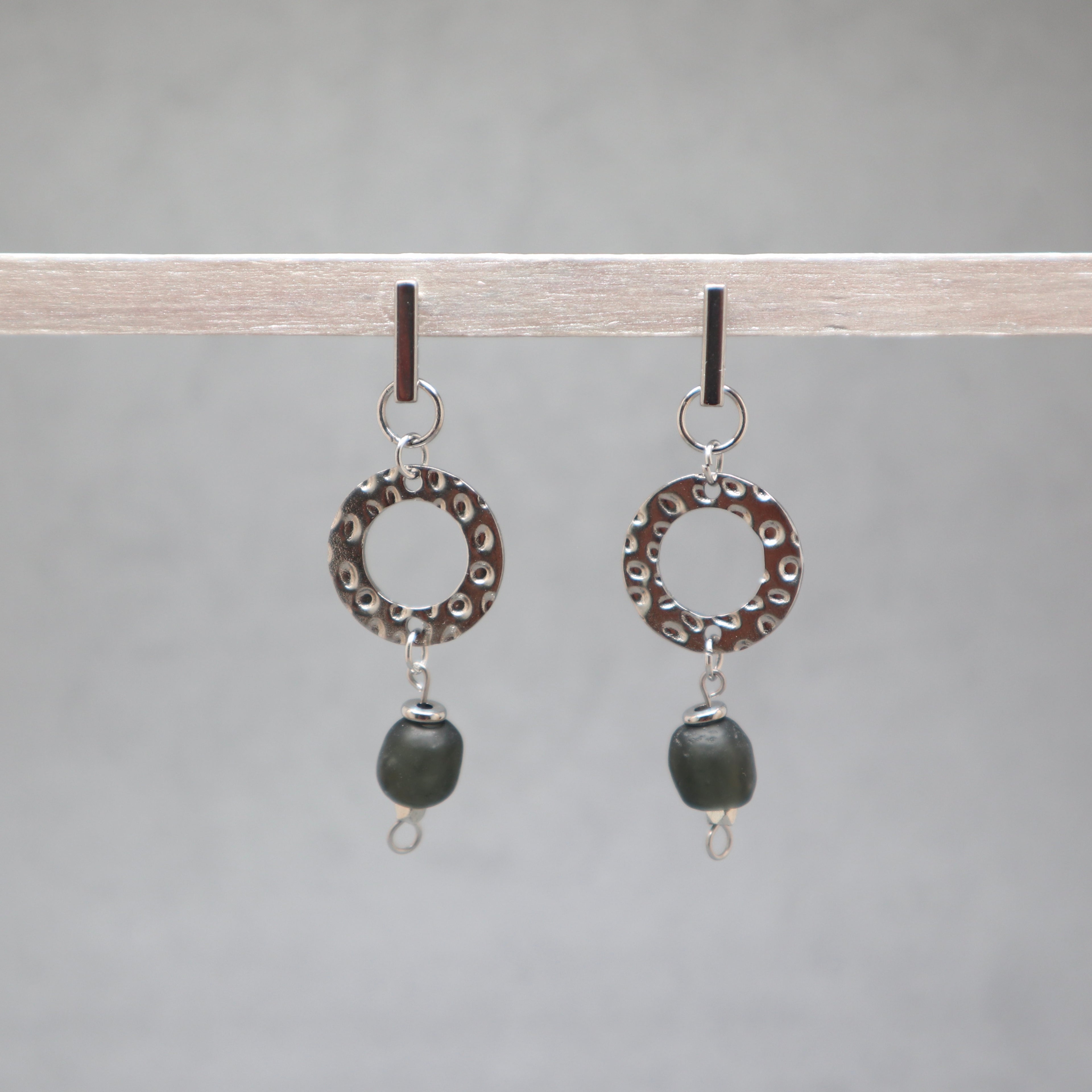 Pair of earrings with circular designs and black beads on a gray background