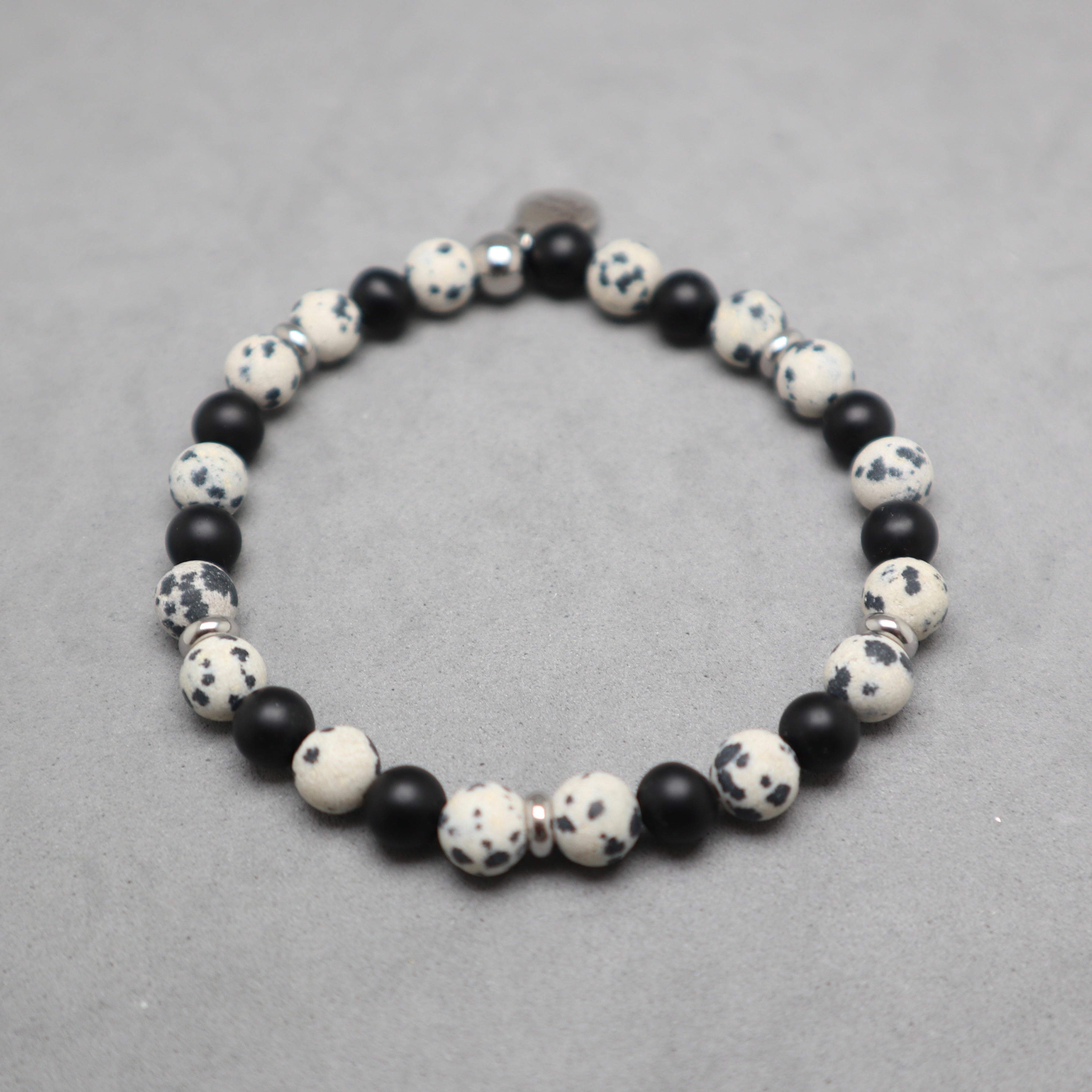 A beaded stretch bracelet featuring alternating matte black beads and speckled white and black stone beads, displayed on a neutral gray textured surface.