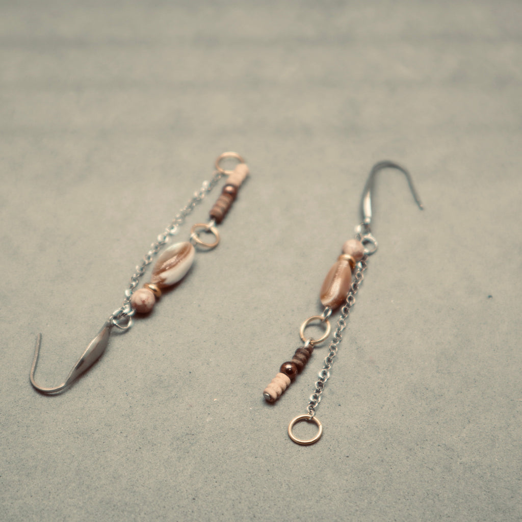 Pair of earrings with shell and bead details on a gray surface