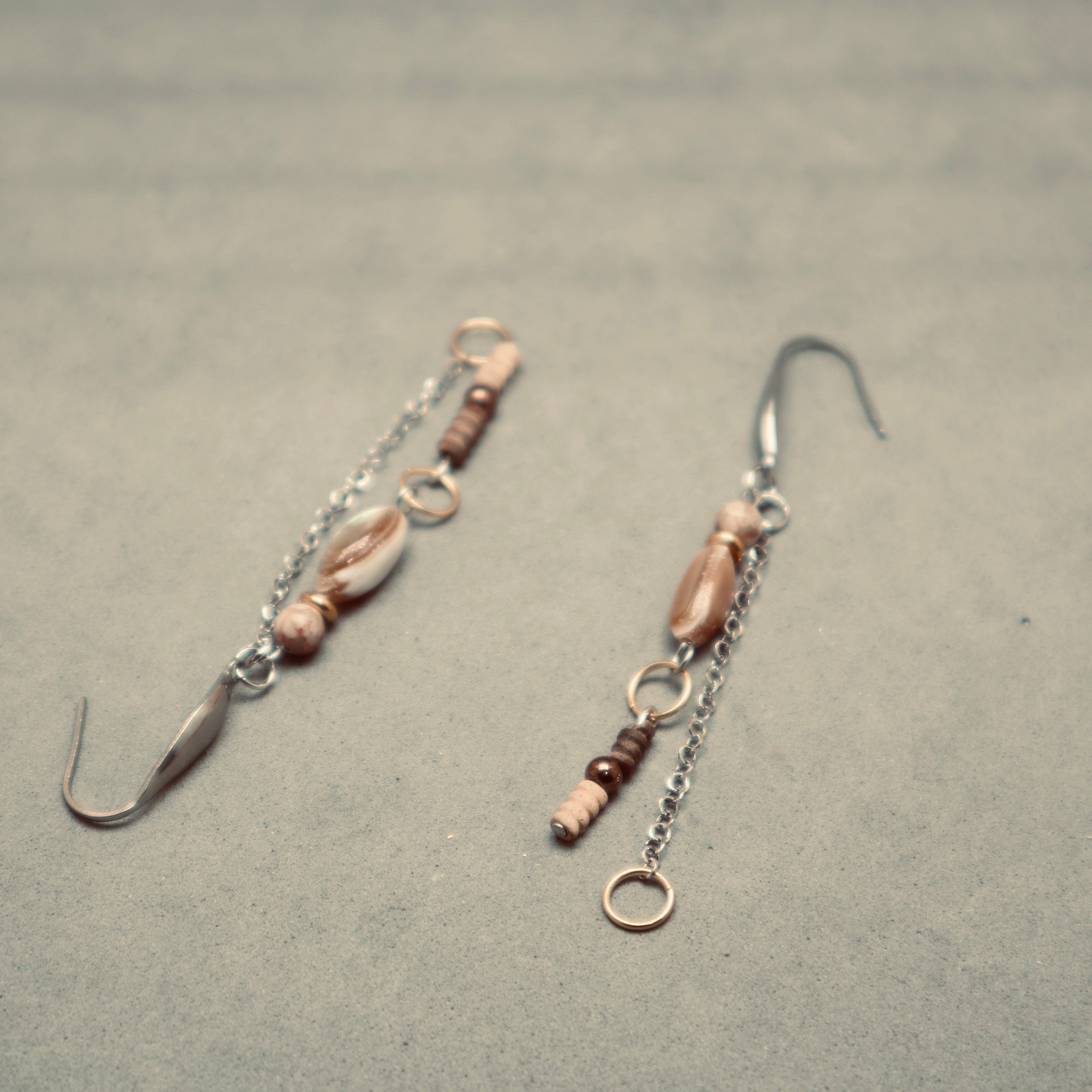Pair of earrings with shell and bead details on a gray surface