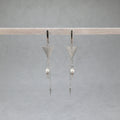 Pair of silver triangle earrings with pearl drops on a gray background