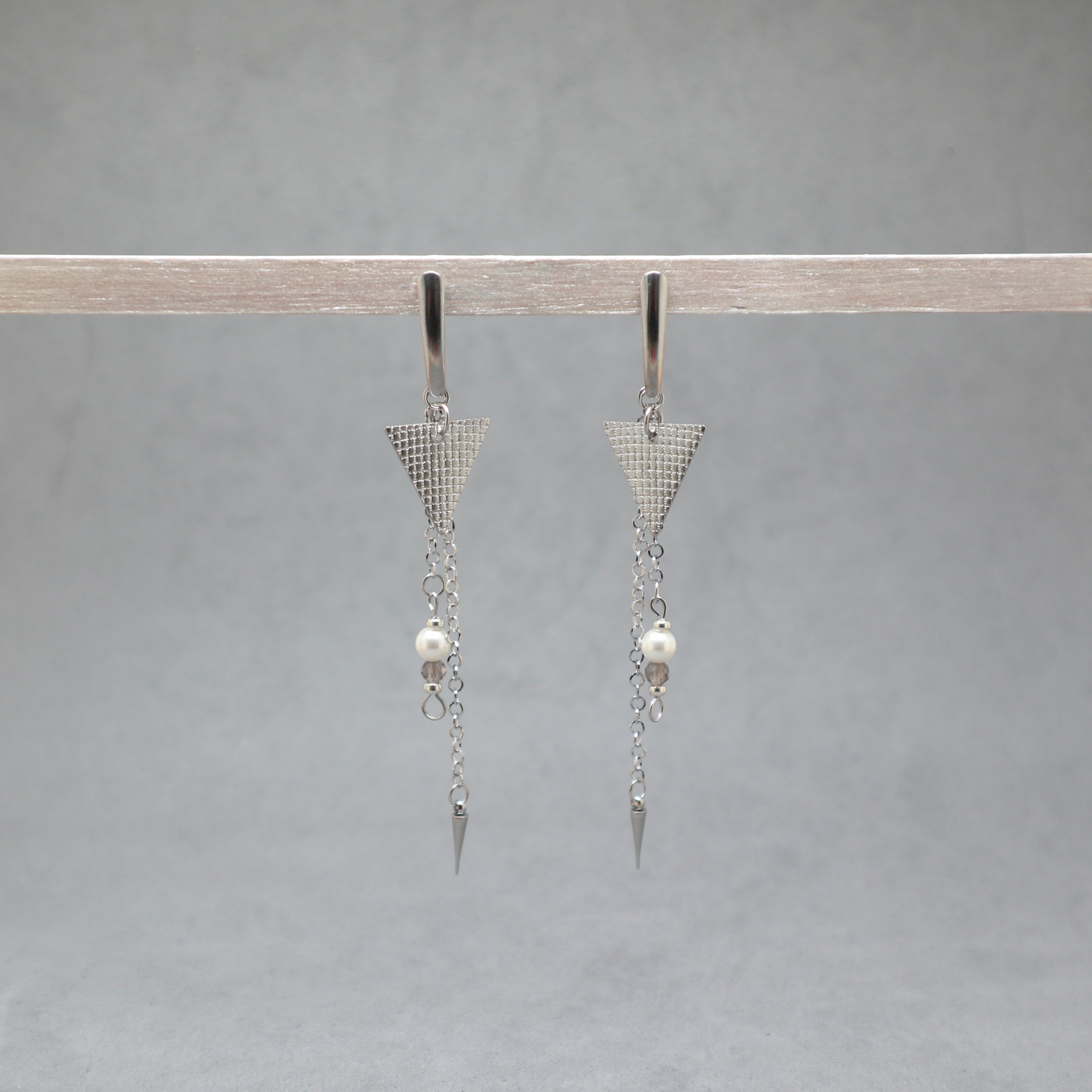 Pair of silver triangle earrings with pearl drops on a gray background