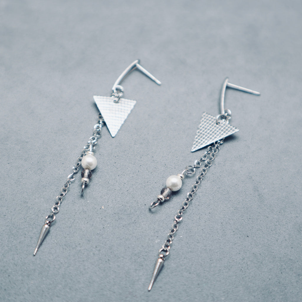 Pair of silver earrings with geometric designs on a gray background