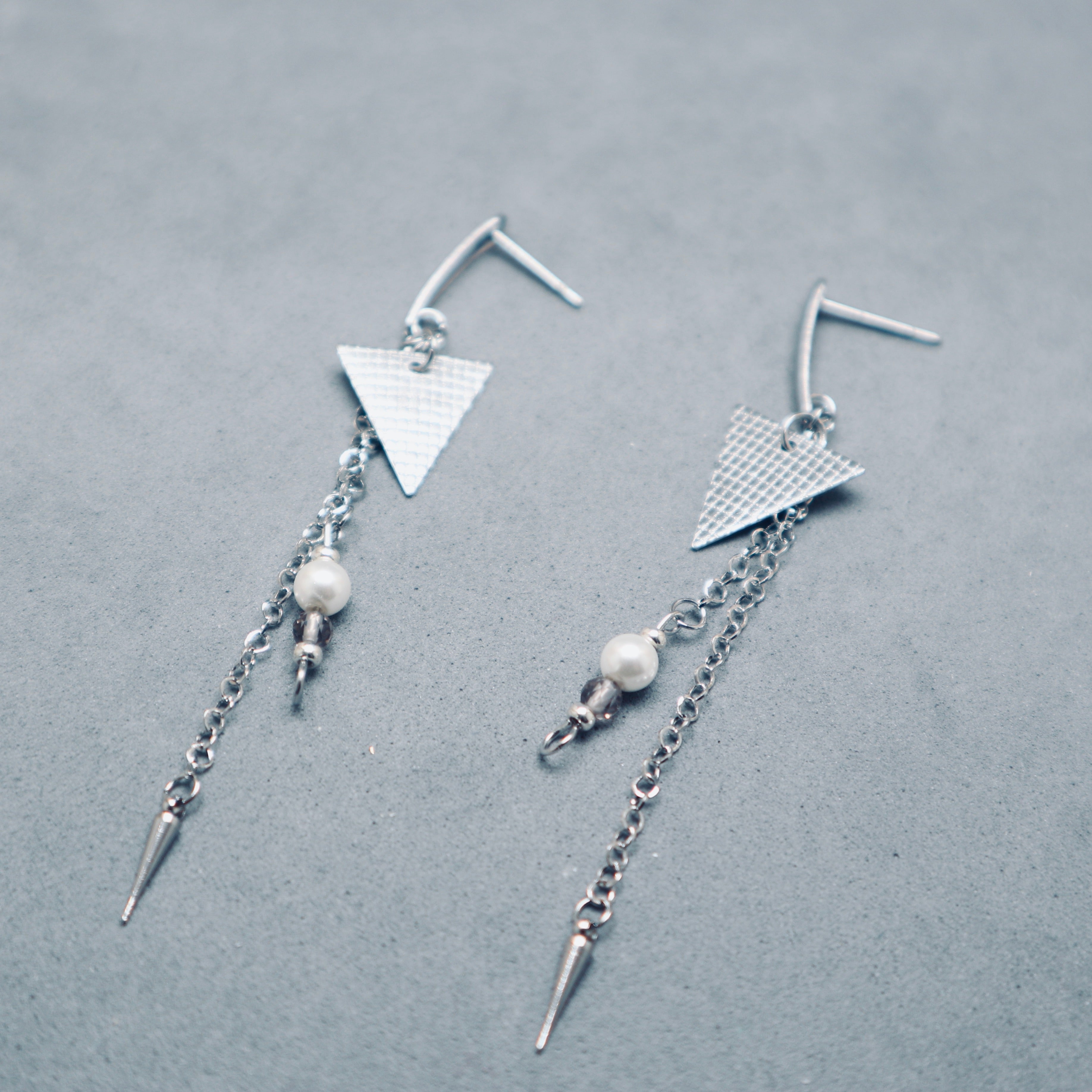 Pair of silver earrings with geometric designs on a gray background