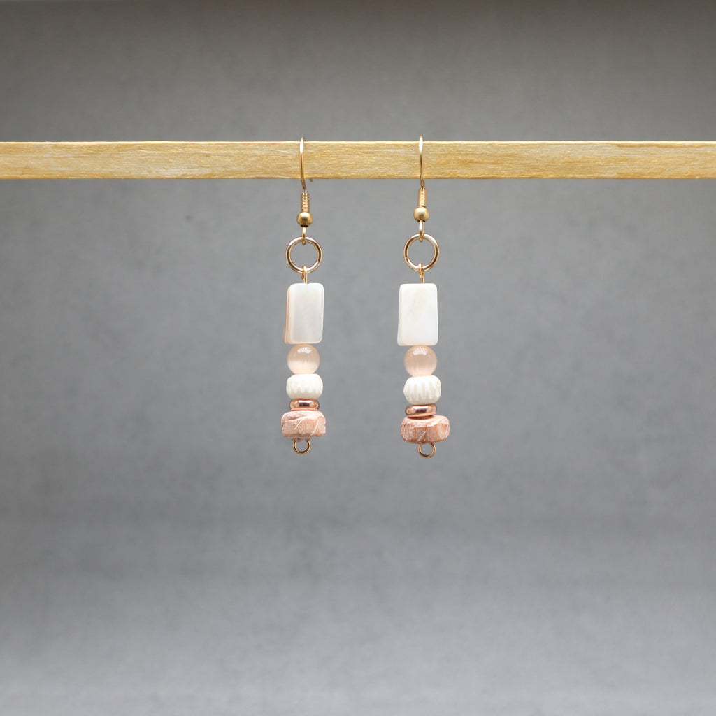 Pair of earrings gold with beads hanging on a wooden rod against a gray background