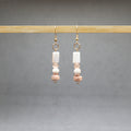 Pair of earrings gold with beads hanging on a wooden rod against a gray background