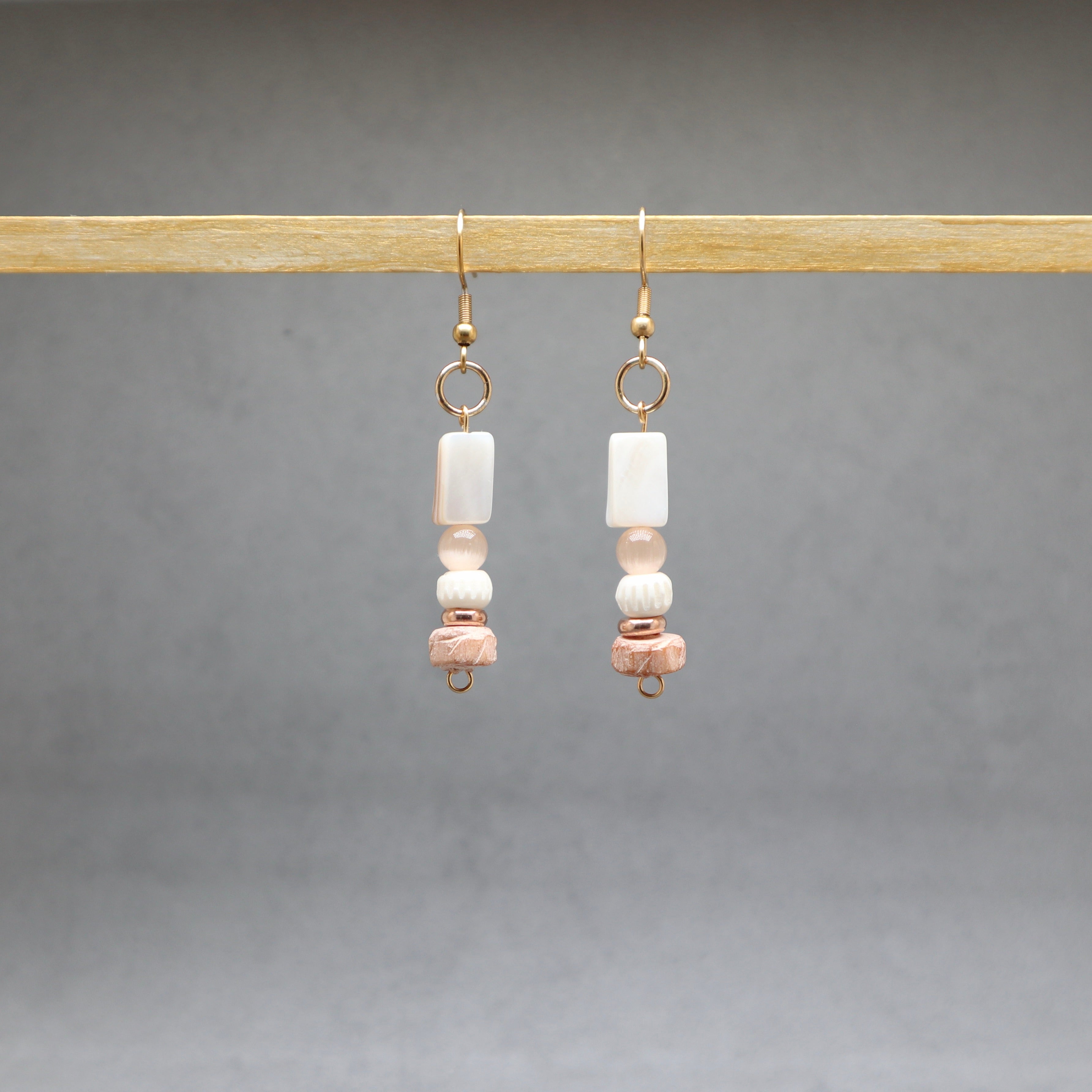 Pair of earrings gold with beads hanging on a wooden rod against a gray background