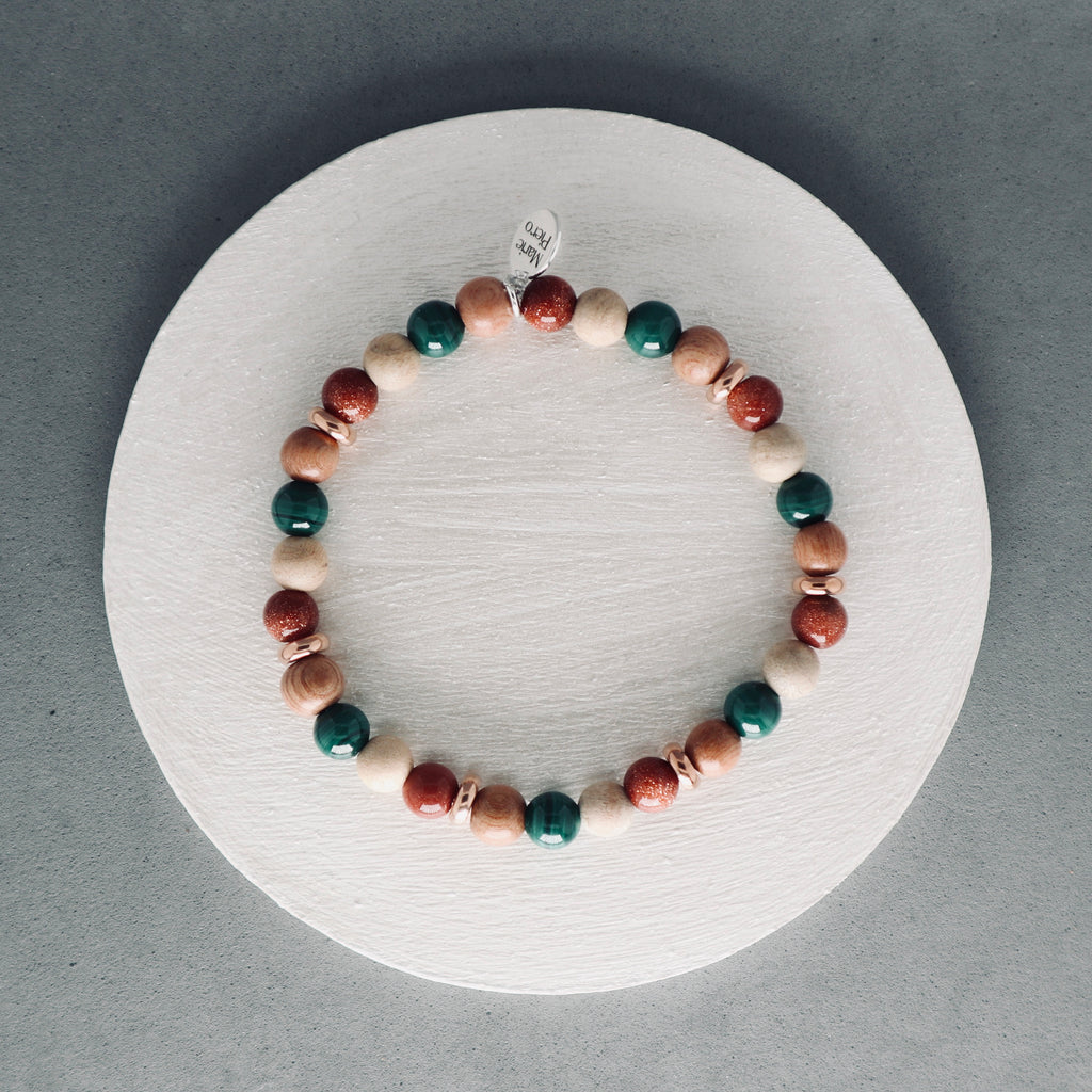 Multicolored beaded bracelet on a white circular stand with a gray background, malachite, rosewood, brown gold stone