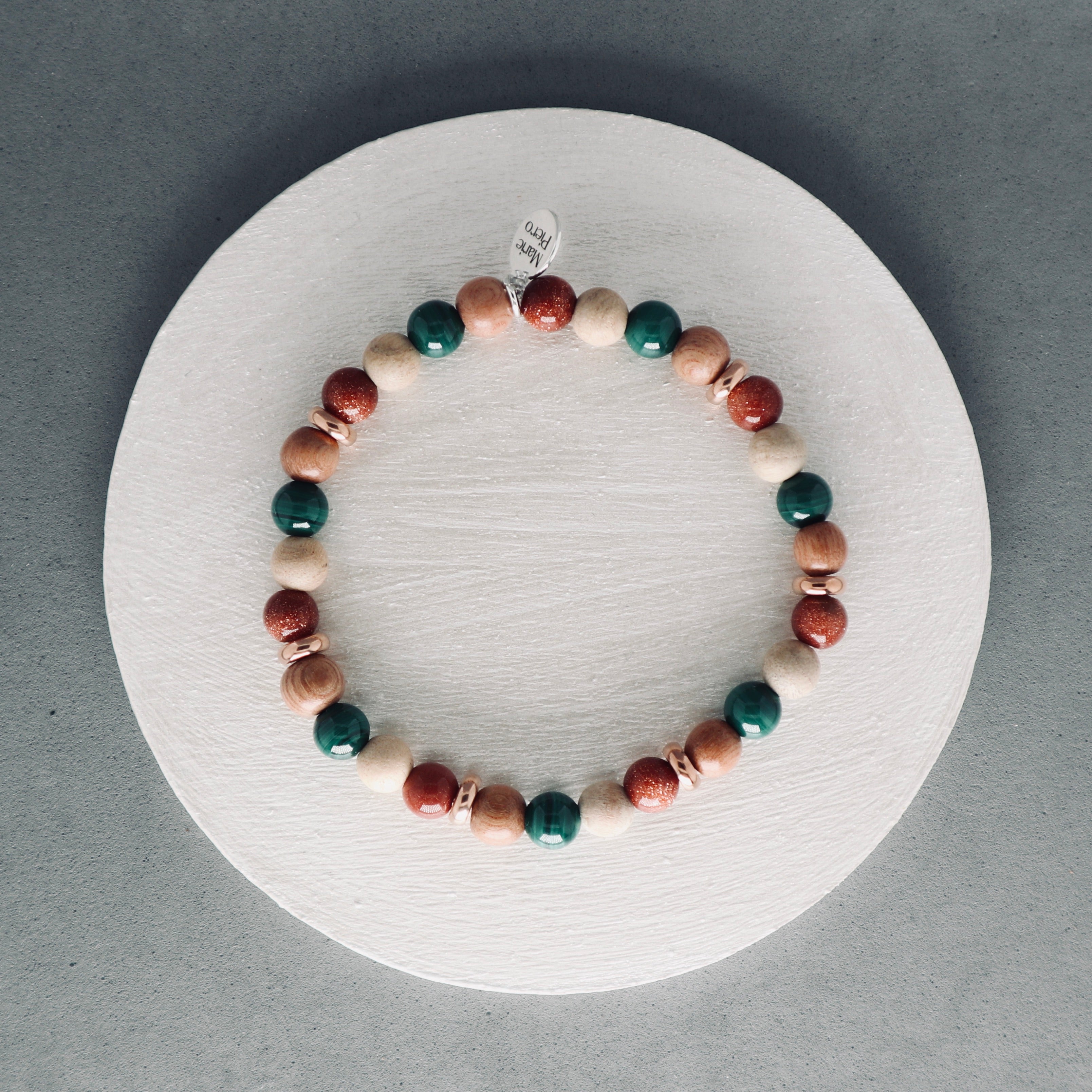 Multicolored beaded bracelet on a white circular stand with a gray background, malachite, rosewood, brown gold stone