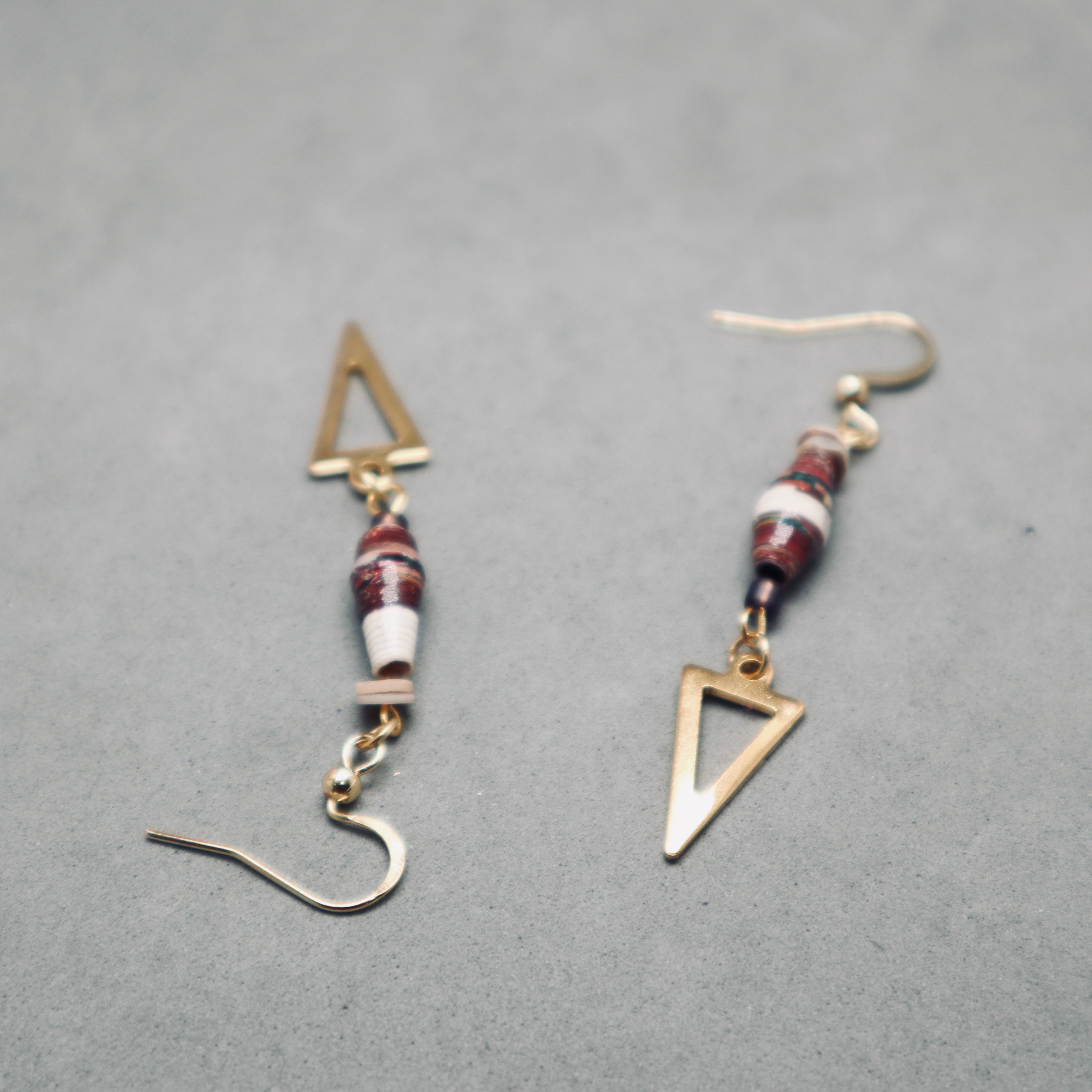 Pair of gold triangle and beaded earrings on a gray background