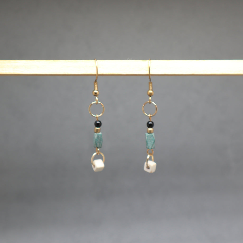 Pair of earrings with beads hanging on a rod against a gray background