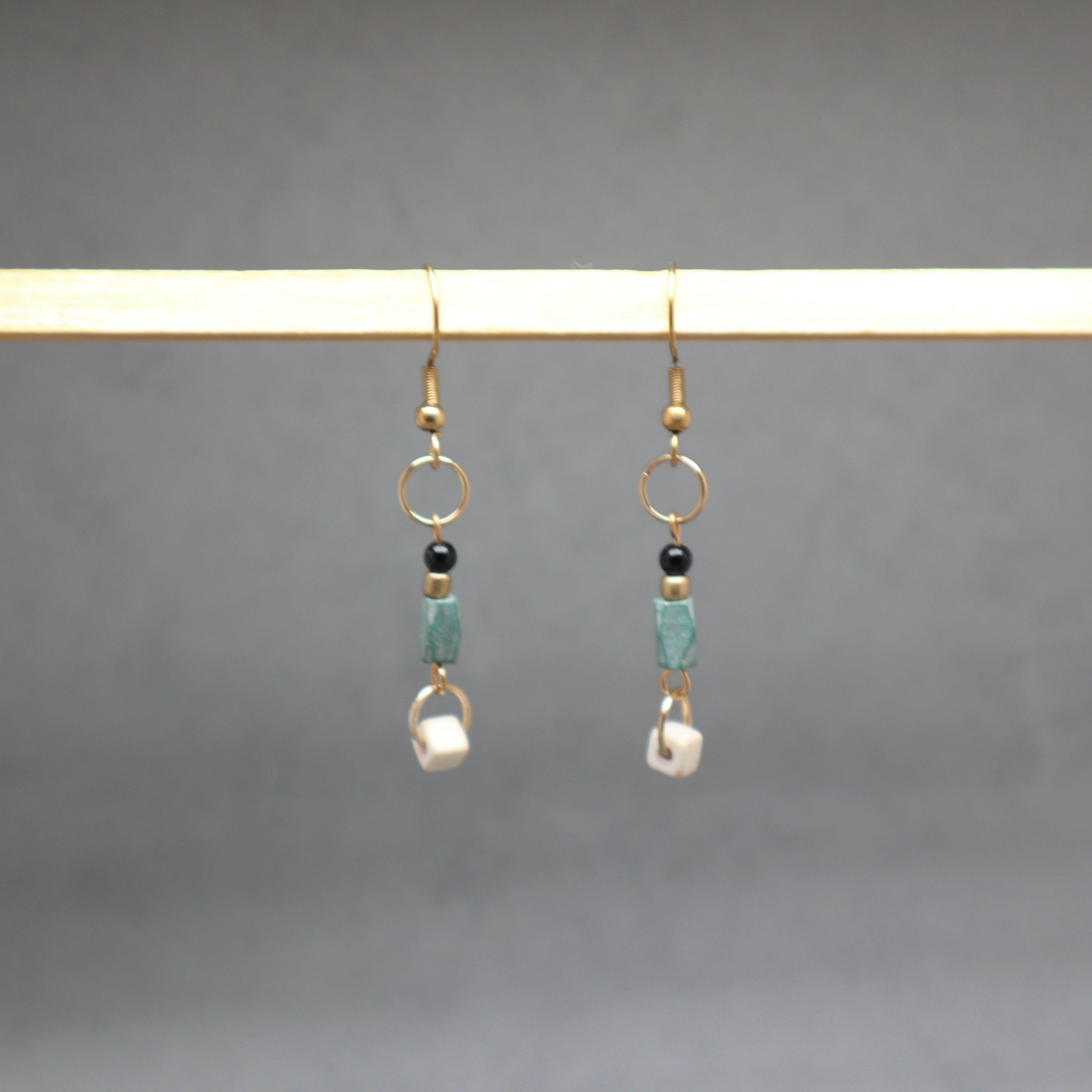 Pair of earrings with beads hanging on a rod against a gray background