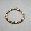 A beaded stretch bracelet featuring natural wood beads, green malachite beads, red coral beads, and small metallic spacer beads, displayed on a neutral gray background.