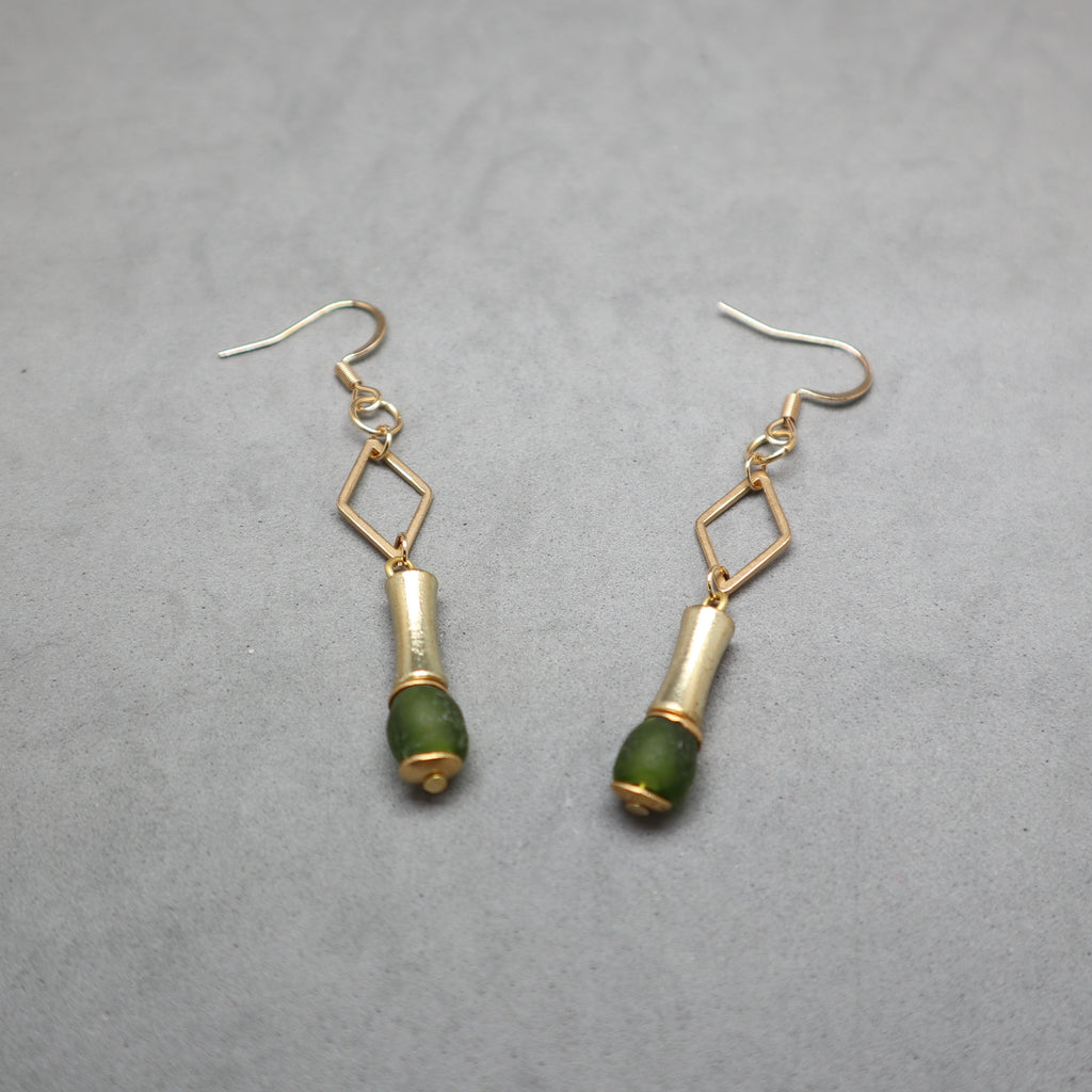 A pair of gold and green drop earrings with geometric diamond-shaped links and cylindrical green bead drops, displayed on a textured gray background.
