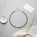 Handmade beaded necklace on a gray surface with a card labeled 'Handmade'., blue, turquoise, women