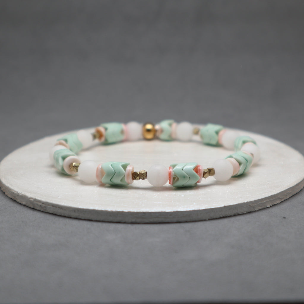 Beaded bracelet with pink, green, and gold accents on a gray background, agate, brass, jade, shell