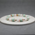 Beaded bracelet with pink, green, and gold accents on a gray background, agate, brass, jade, shell