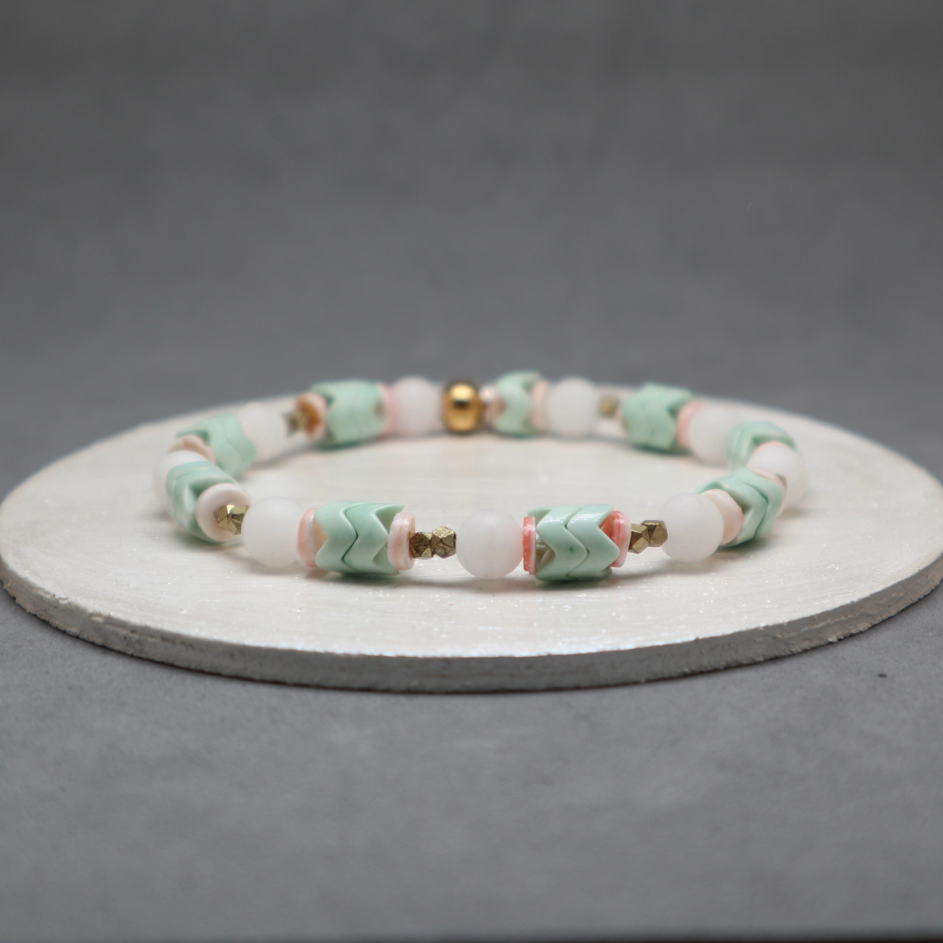 Beaded bracelet with pink, green, and gold accents on a gray background, agate, brass, jade, shell